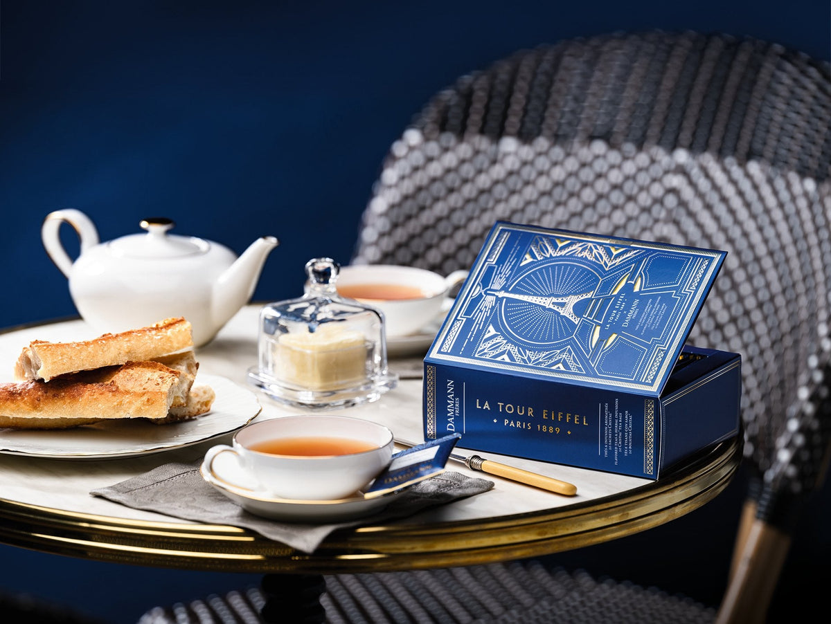 Coffret Dammann Frères La Tour Eiffel sur une table de bistrot parisien, avec théière, tasses et pain grillé