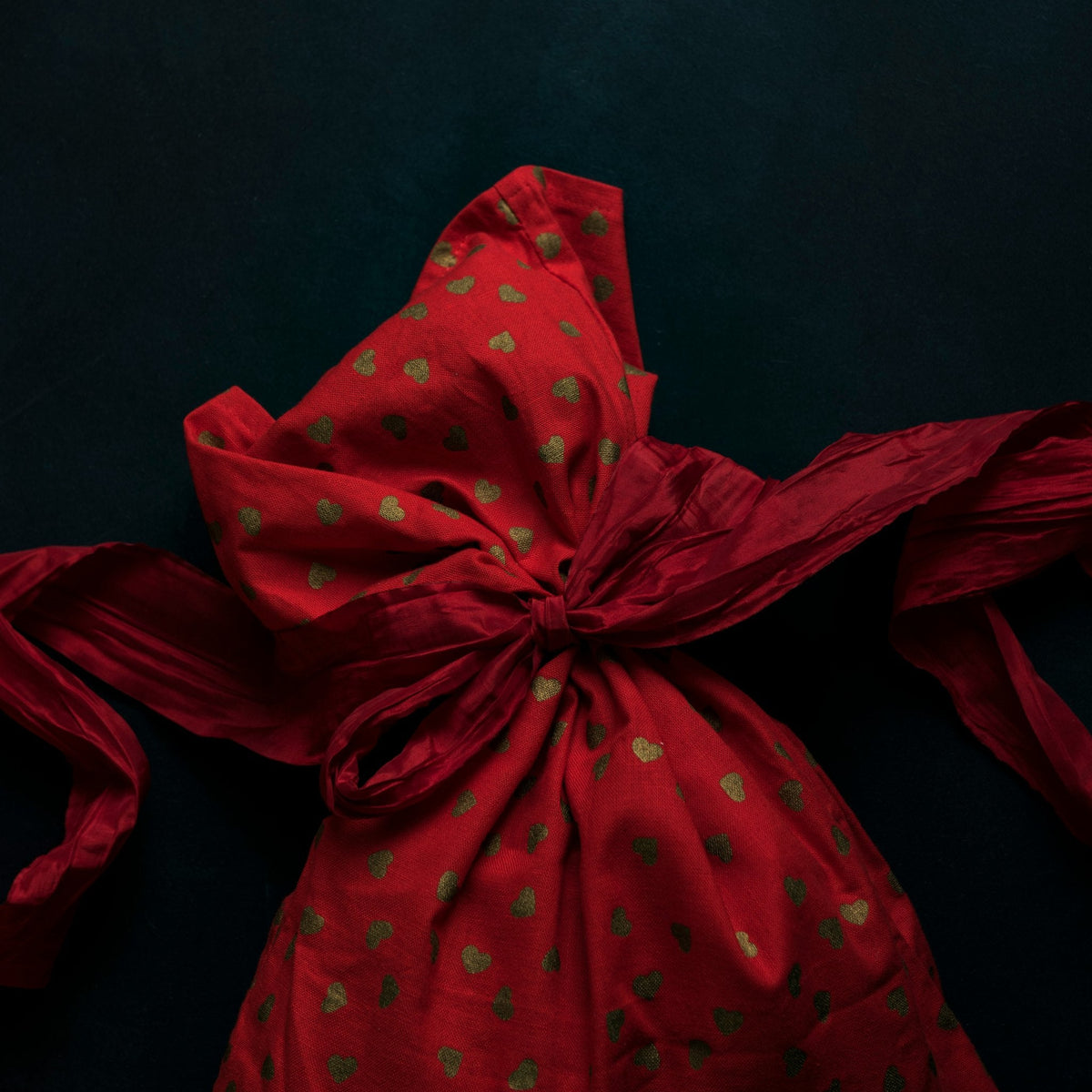 Red gift bag with gold hearts tied with a red ribbon on a dark background