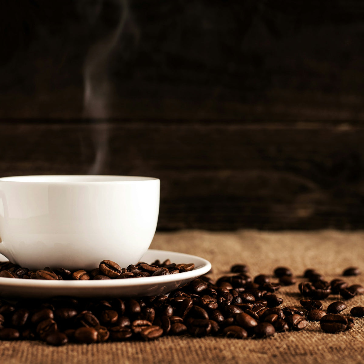 Steaming white cup of coffee on a saucer with roasted coffee beans
