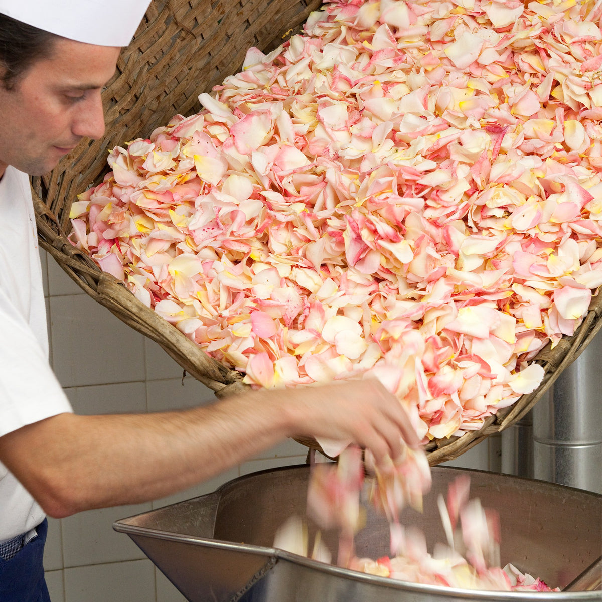A Confiserie Florian confectioner pouring fresh rose petals into a cooking basin