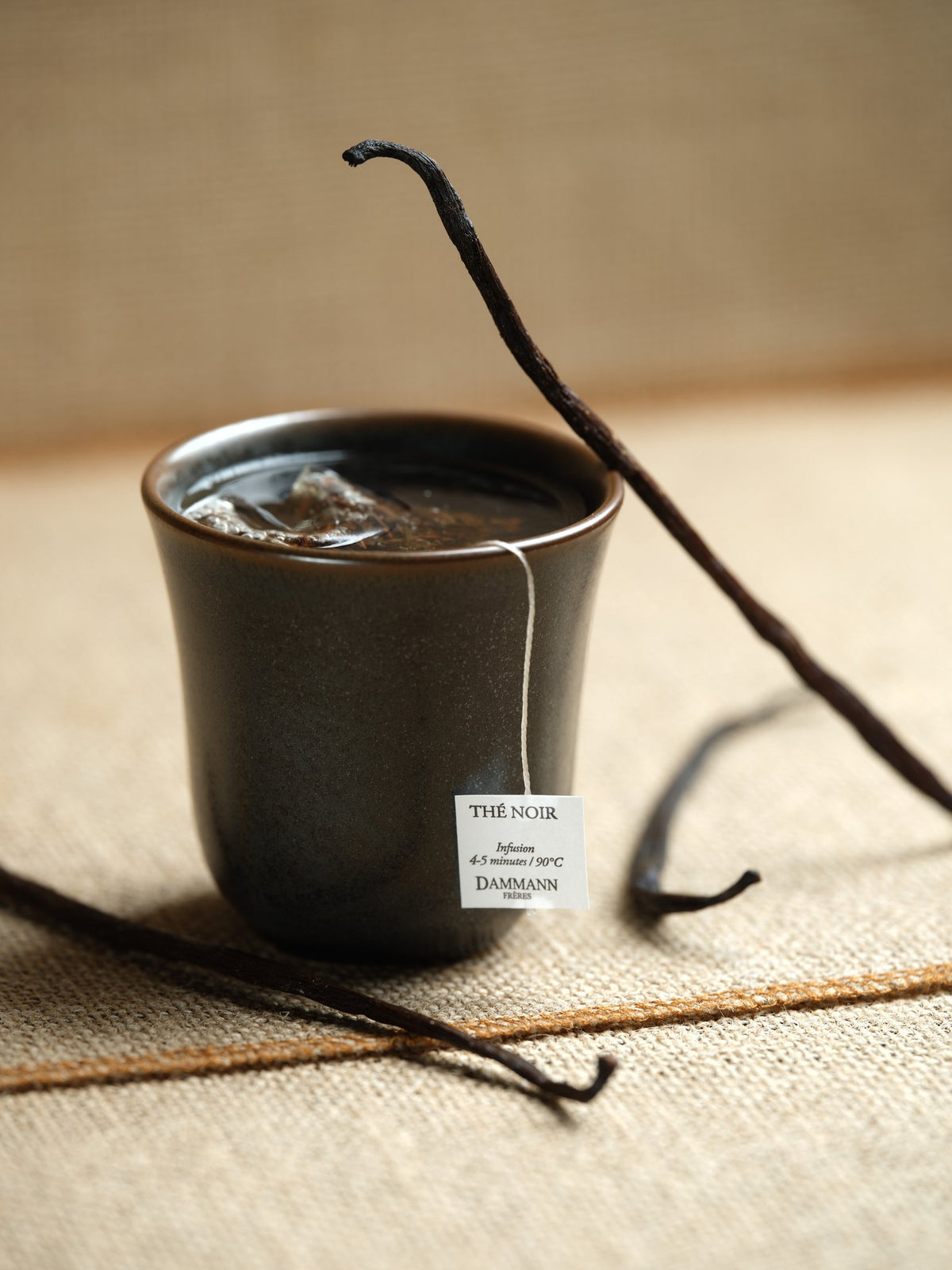 Sachet de thé bio à la vanille infusant dans une tasse, à côté de gousses de vanille