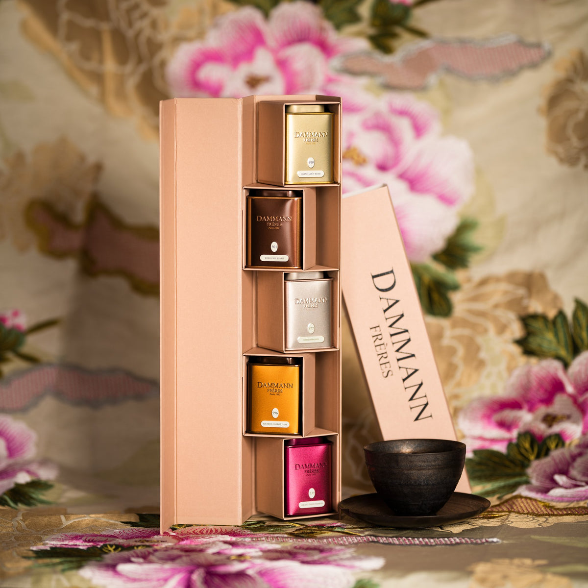 Dammann Frères Iris gift box open with five tea tins beside a tea bowl on floral fabric