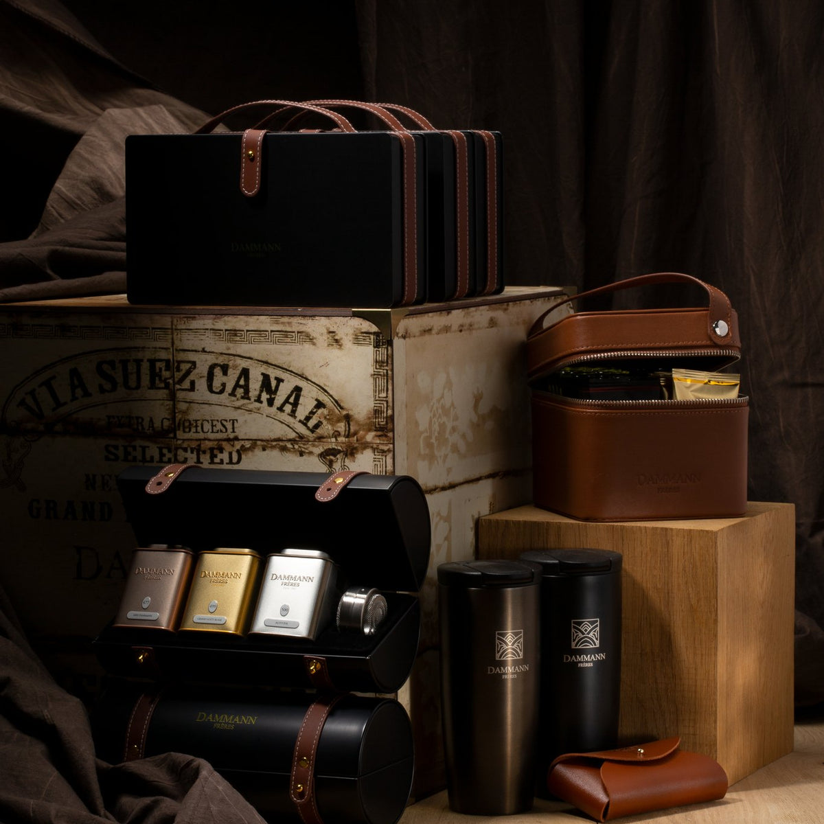 Dammann Frères Merveilleux black strapped case open with three tea tins and an infuser, beside a vintage tea chest