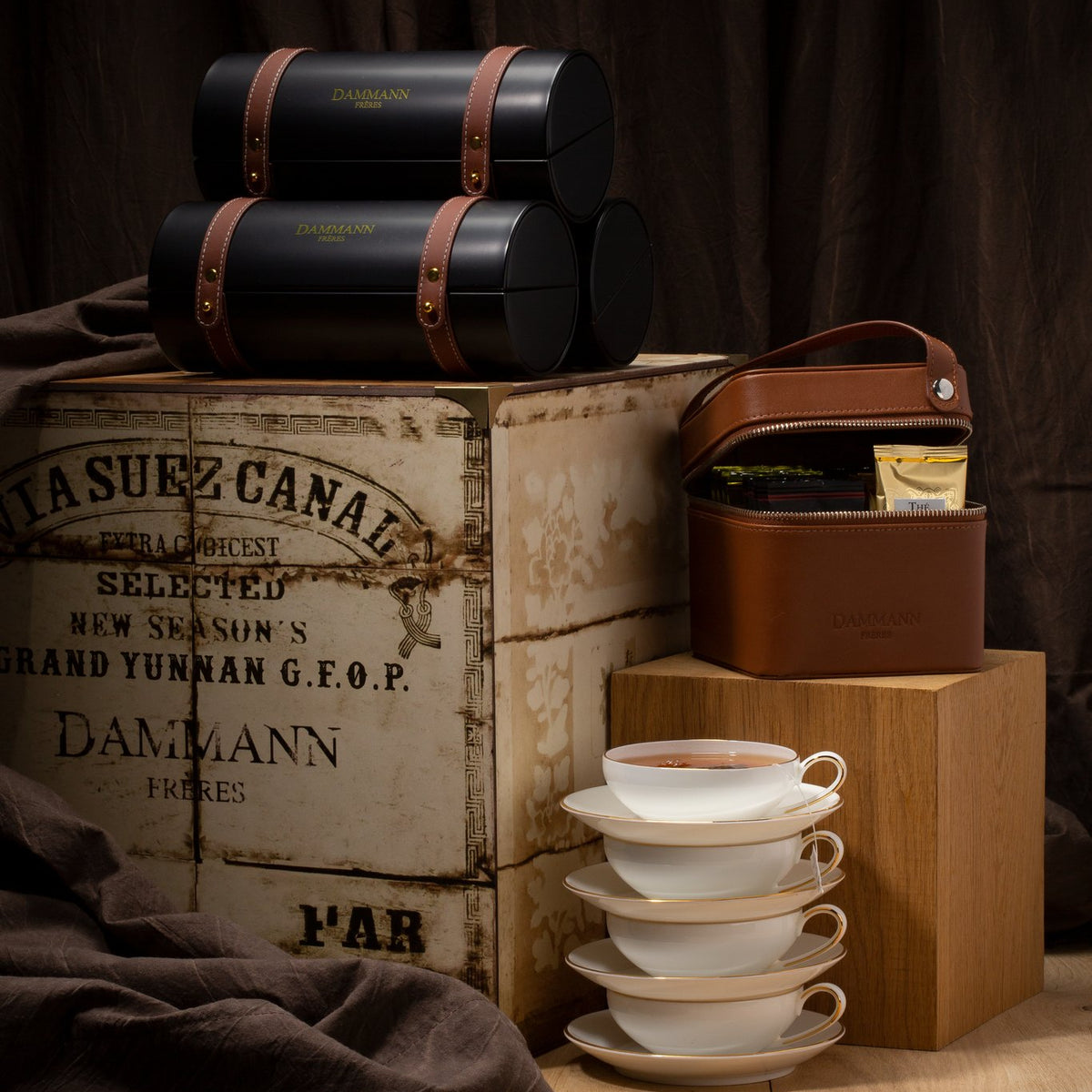 Dammann Frères Merveilleux black cylinder gift boxes with leather straps on a vintage tea chest