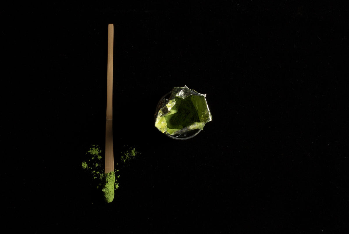 Chashaku by Dammann Frères, bamboo matcha scoop with a sprinkle of matcha powder on a black background