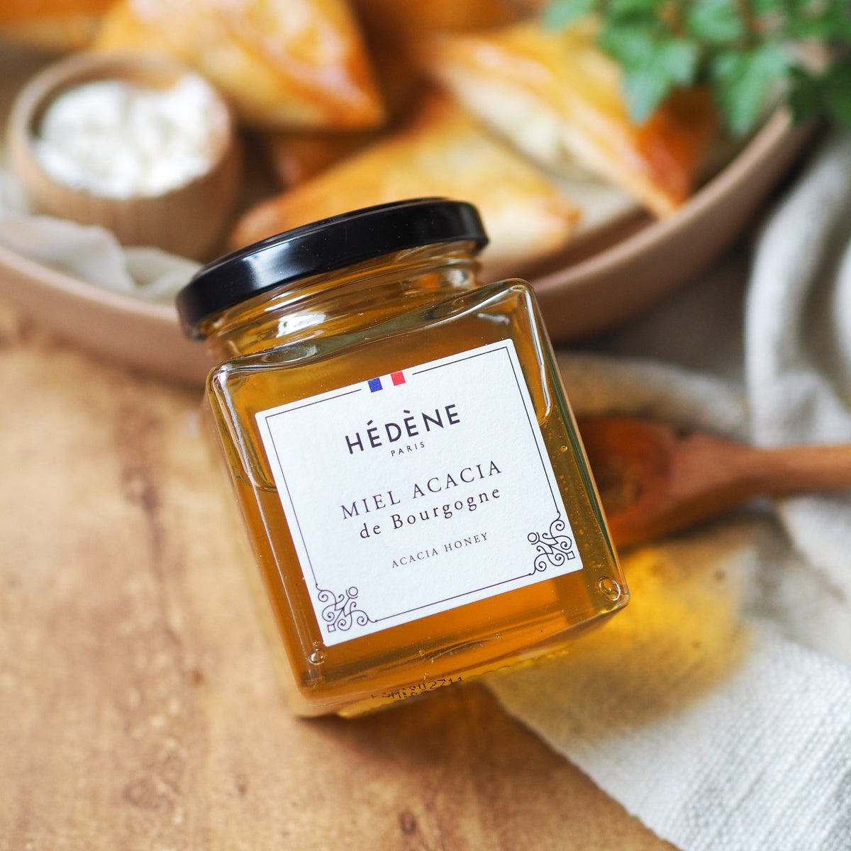 Pot de miel d’acacia Hédène sur une planche en bois avec des tapas