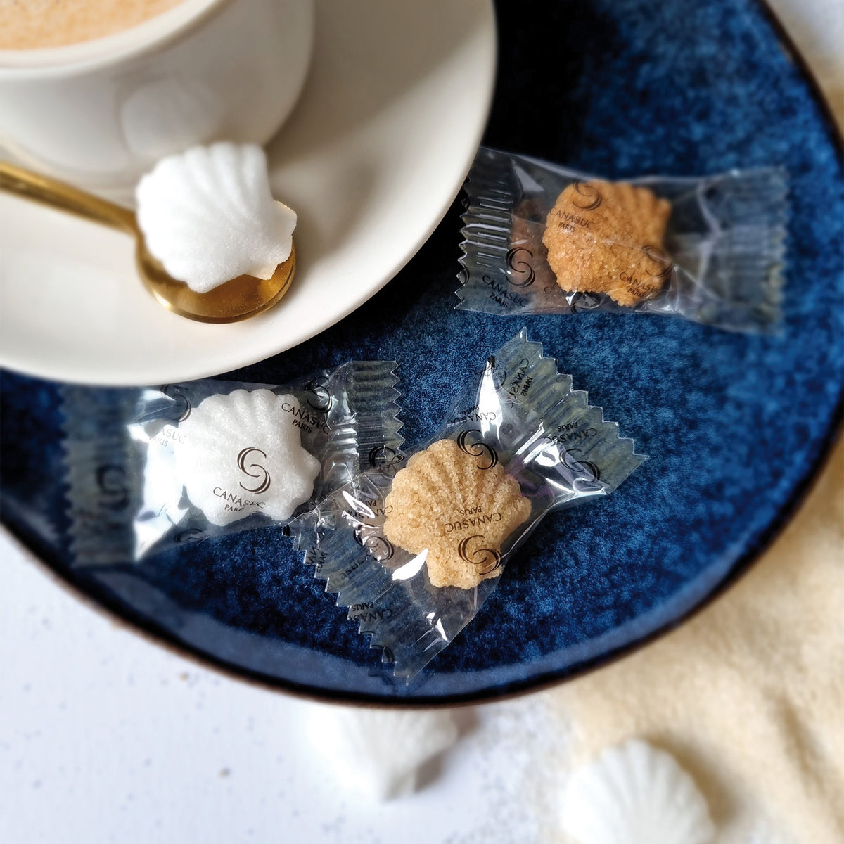 Sucres en coquille Saint-Jacques Prendre le large Canasuc dans leurs sachets individuels, à côté d’un café
