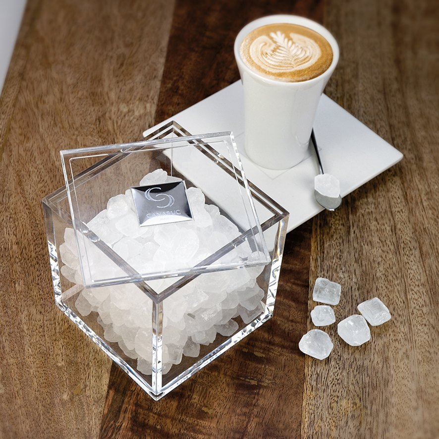 Canasuc white candy sugar in a clear cube box beside a coffee