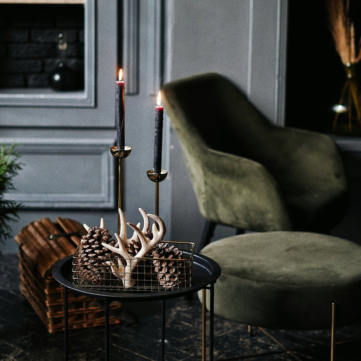 Candlelit living room with a green velvet armchair and pine cones
