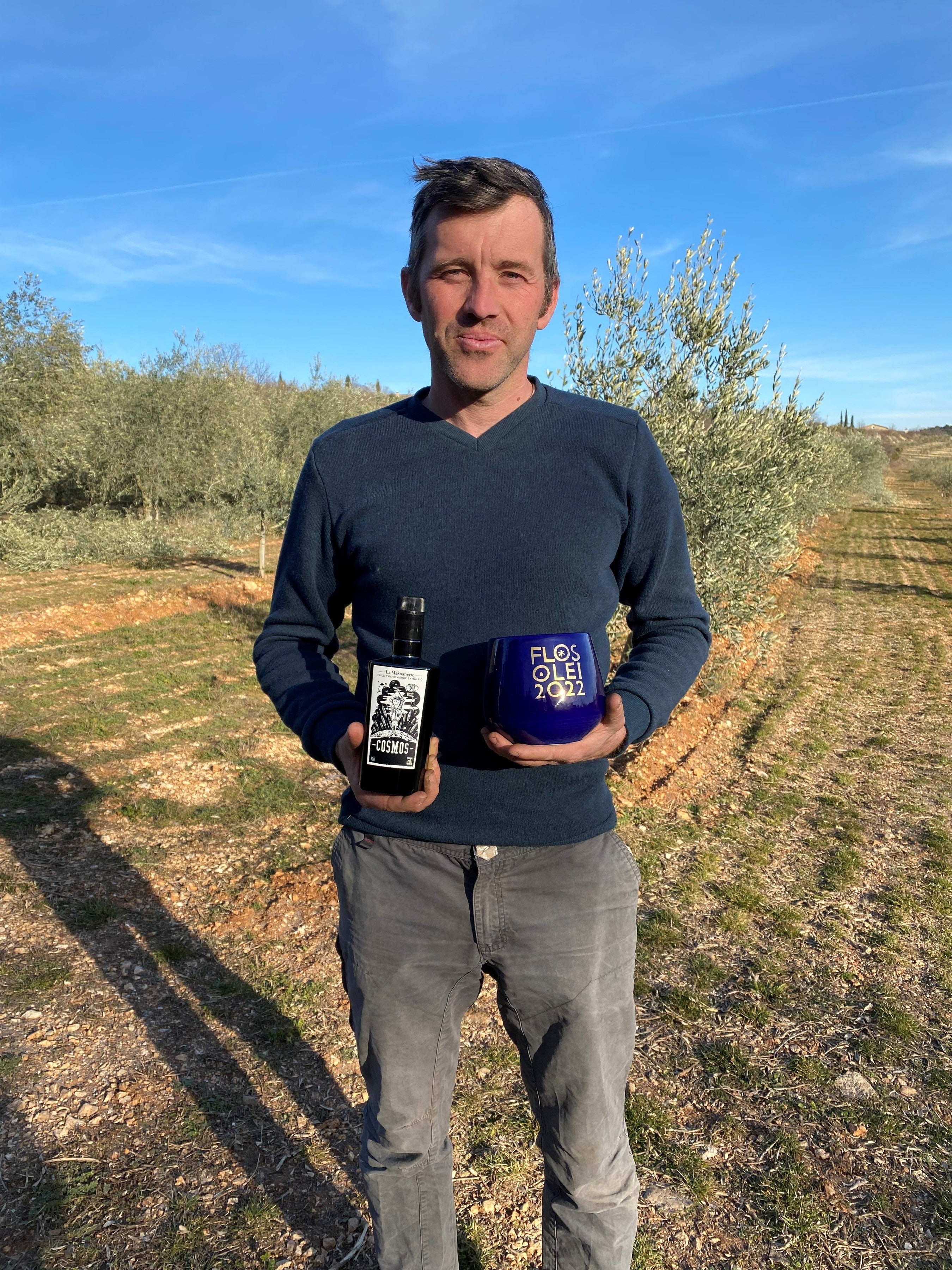 Olive grower of La Magnanerie in the estate's Ardèche groves, holding a bottle and a tin of olive oil