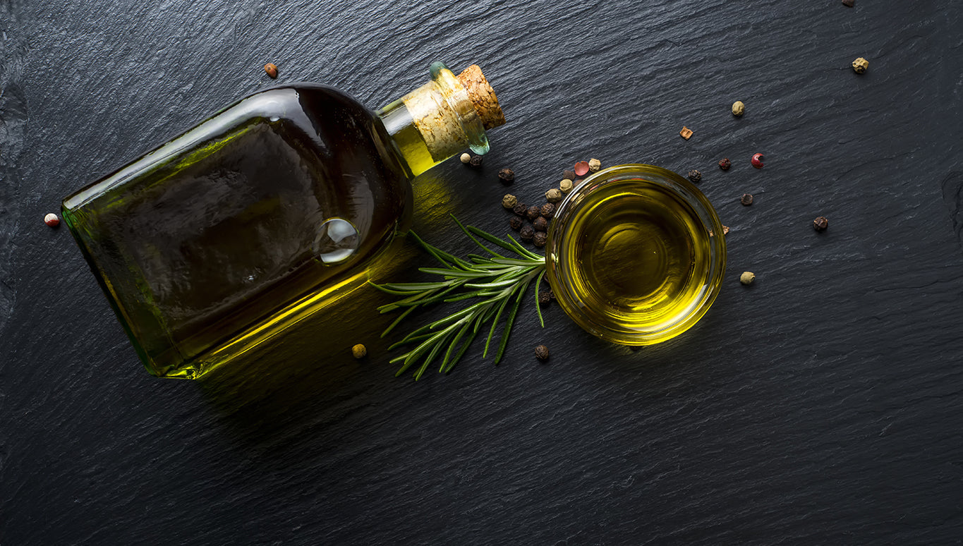 Bottle of olive oil with a sprig of rosemary and peppercorns on dark slate