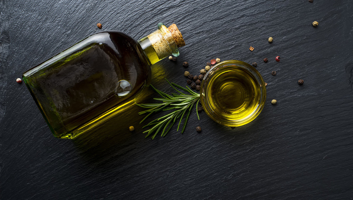 Bottle of olive oil with a sprig of rosemary and peppercorns on dark slate