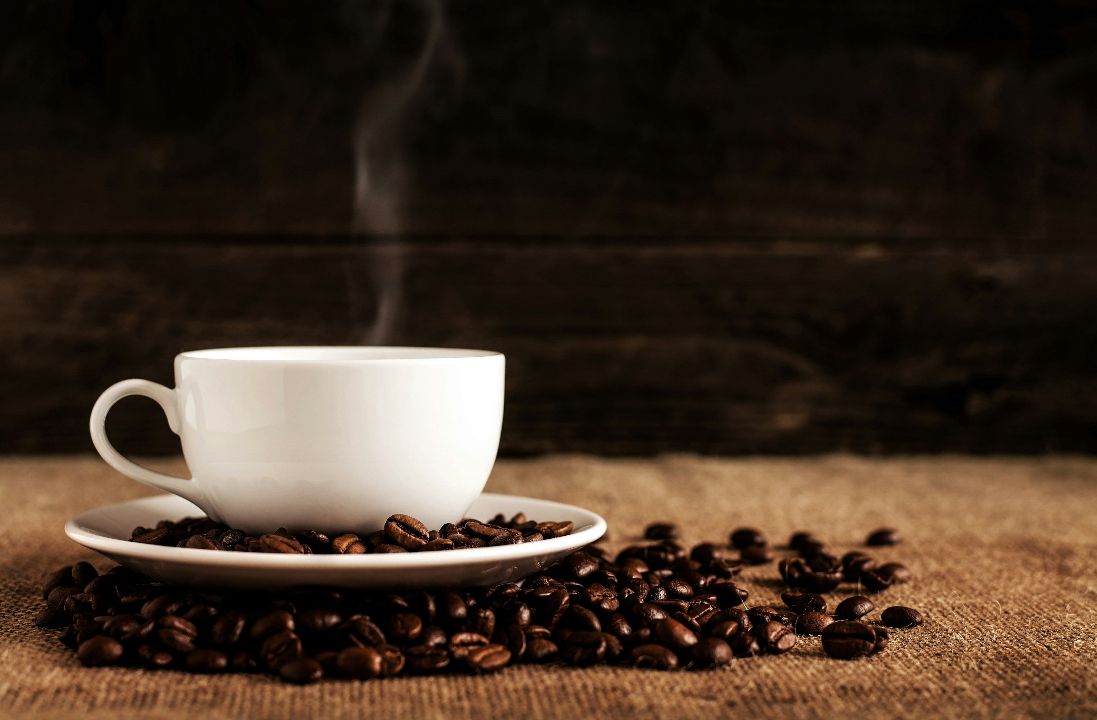 Steaming white cup of coffee on a saucer with roasted coffee beans