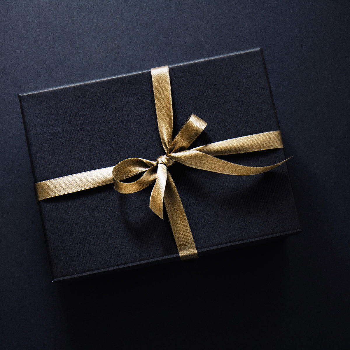 Black gift box tied with a gold satin ribbon
