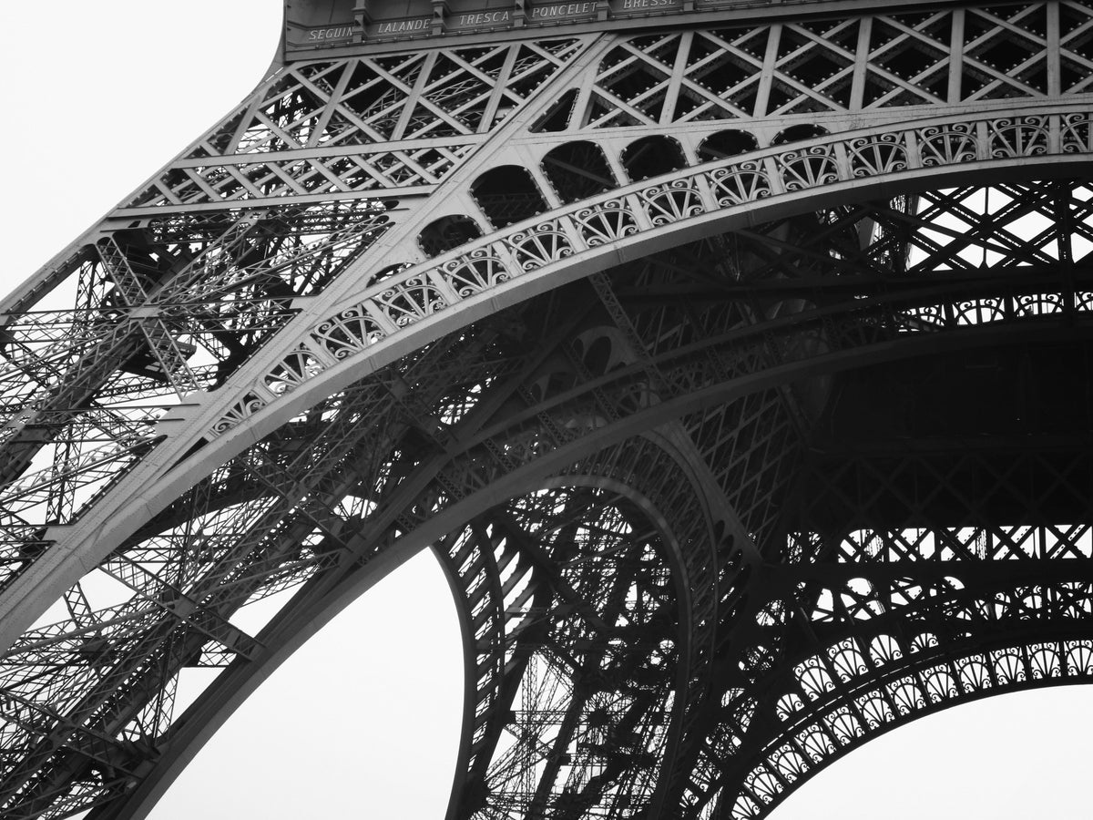 Vue en noir et blanc du treillis de fer de la tour Eiffel, en contre-plongée