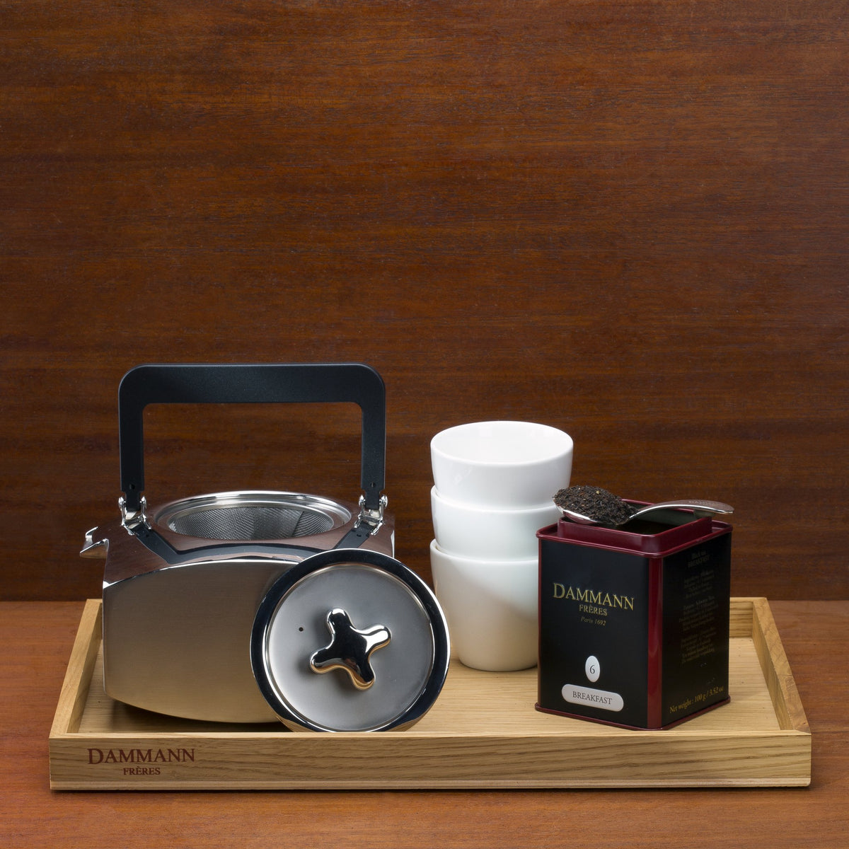 Dammann Frères Breakfast N°6 tea tin with a steel kettle and white cups on an engraved oak tray