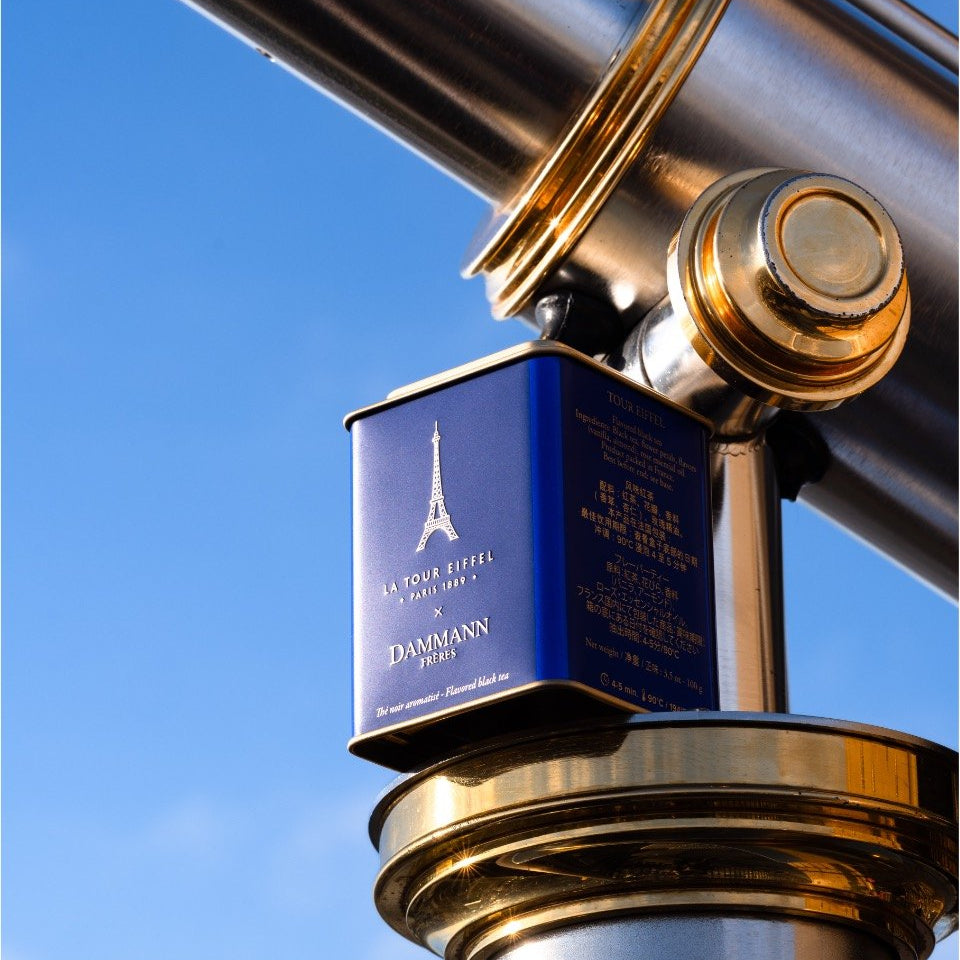 Boîte de thé bleue La Tour Eiffel de Dammann Frères sur une longue-vue en laiton, sur fond de ciel bleu