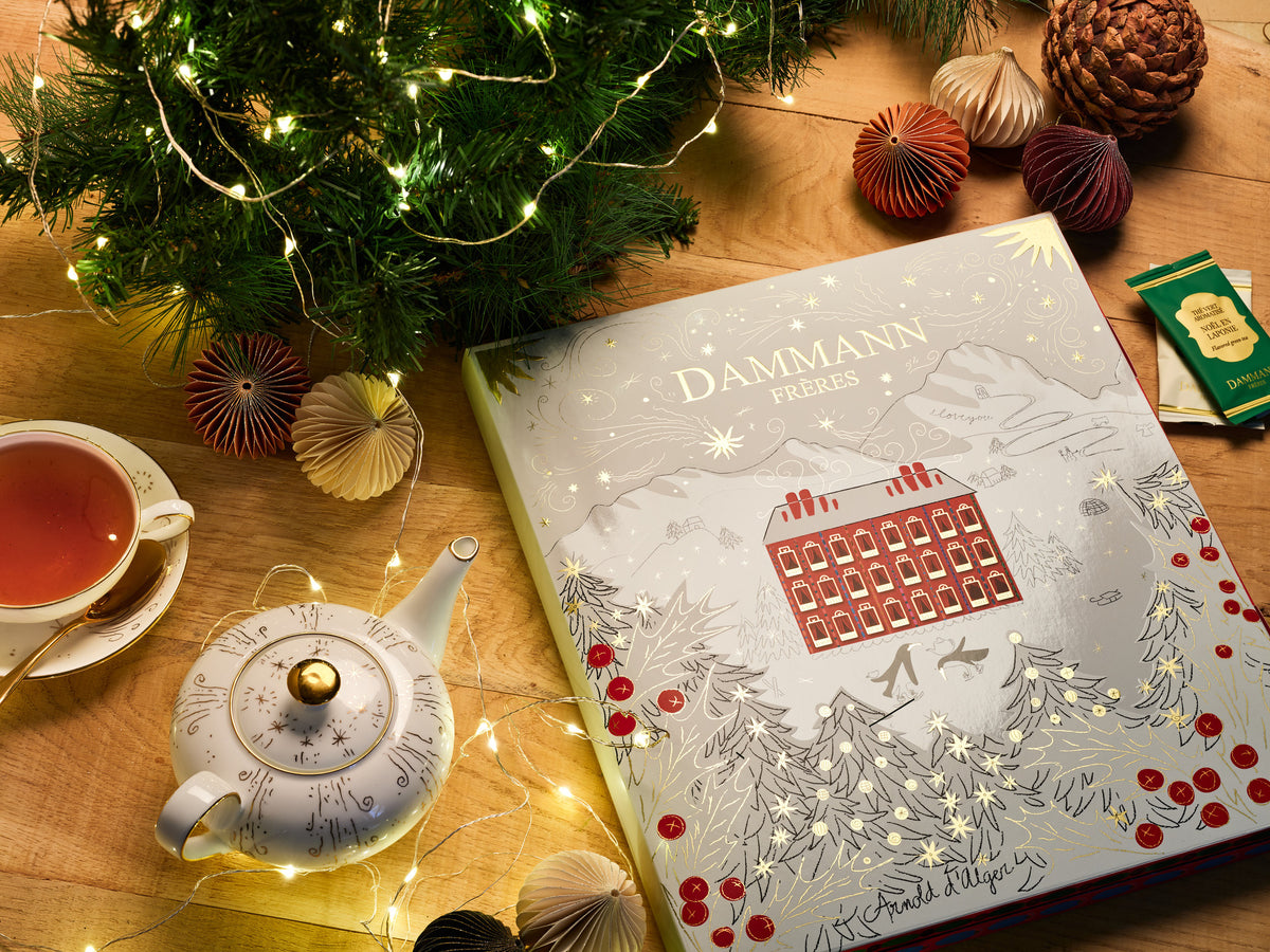 Calendrier de l’Avent Dammann Frères sur une table en bois avec une théière, une tasse de thé et des décorations de Noël