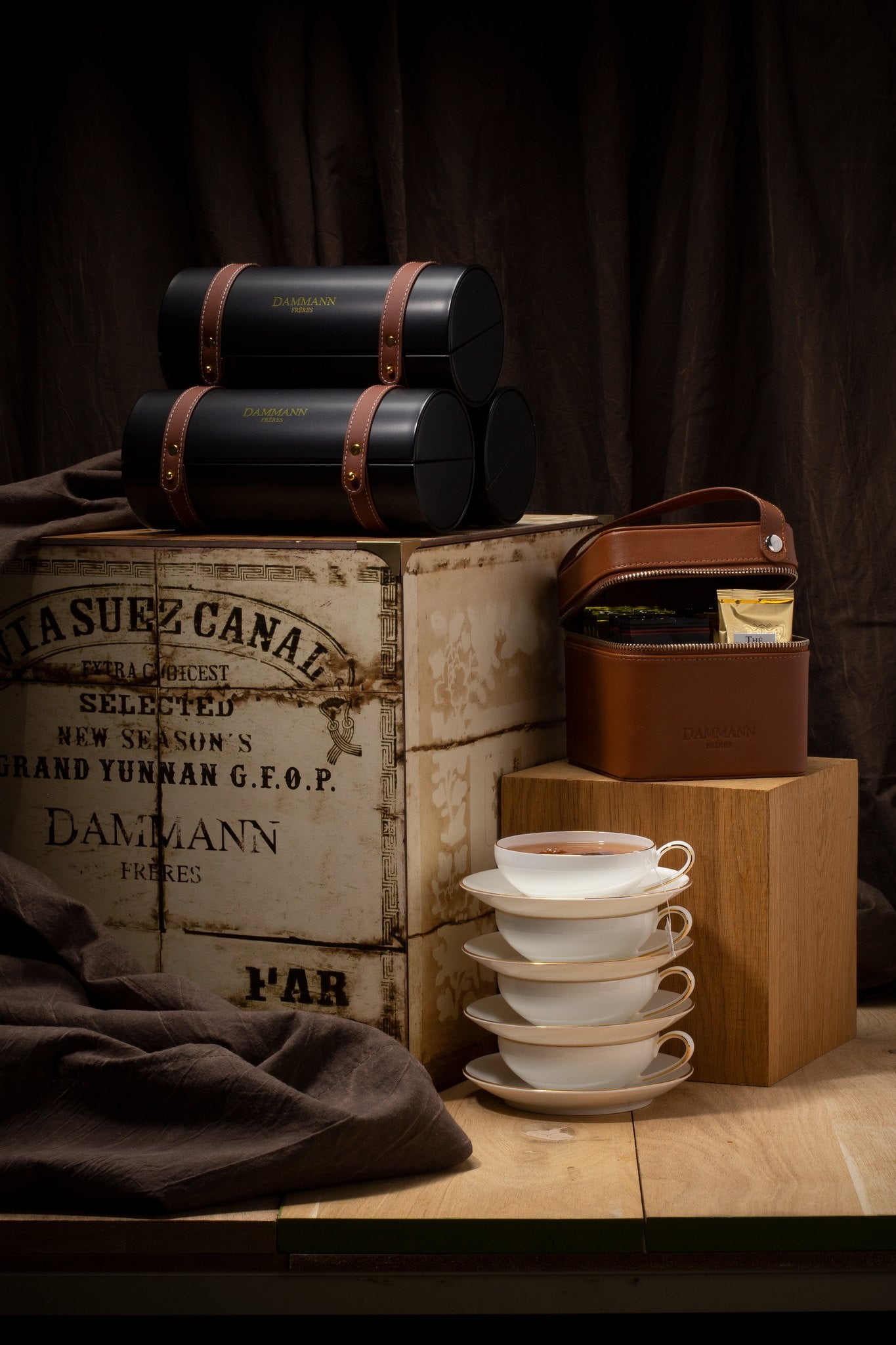 Dammann Frères Merveilleux black cylinder gift boxes with leather straps on a vintage tea chest