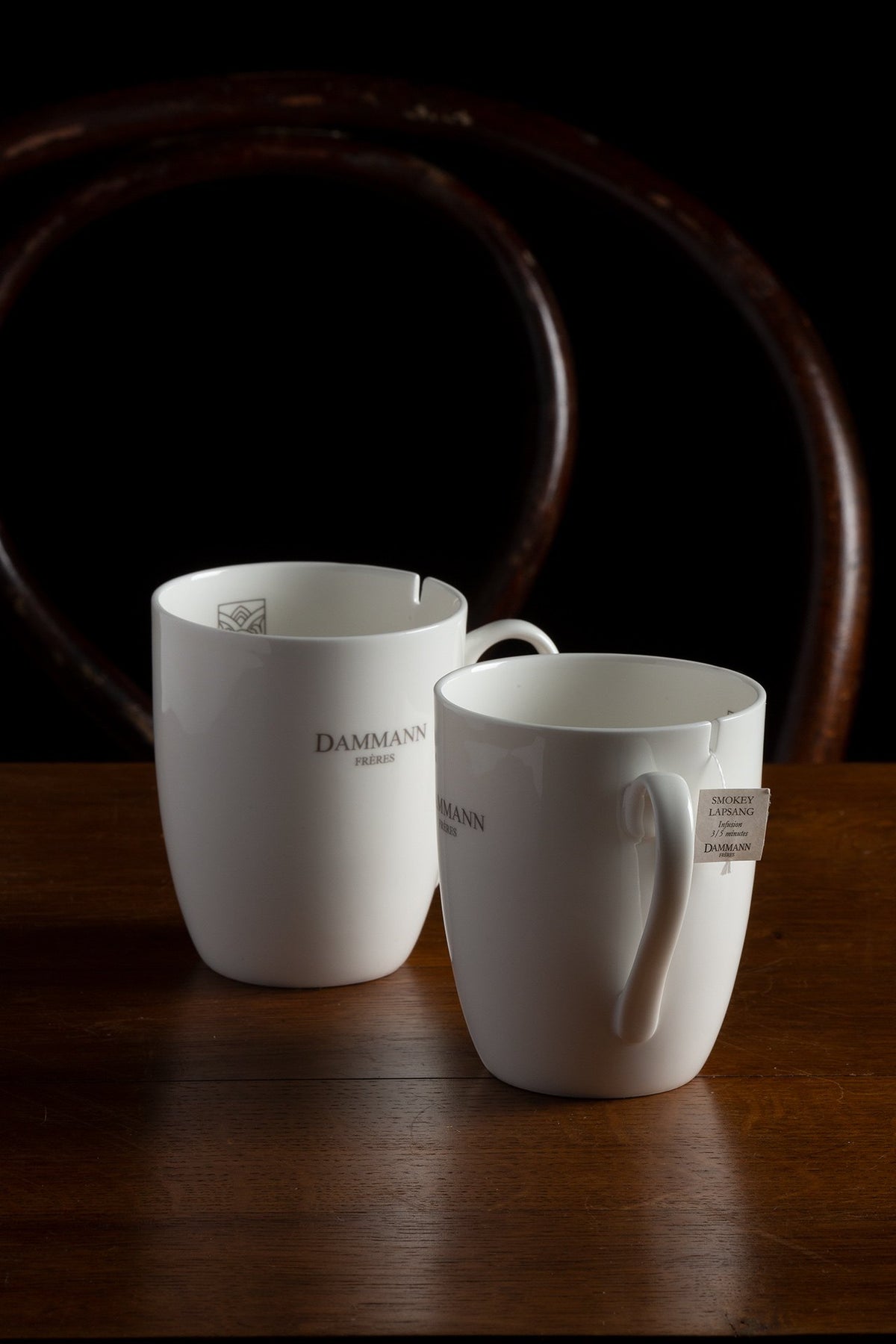 Two white Dammann Frères hotel mugs, one with a tea bag tag, on a wooden table
