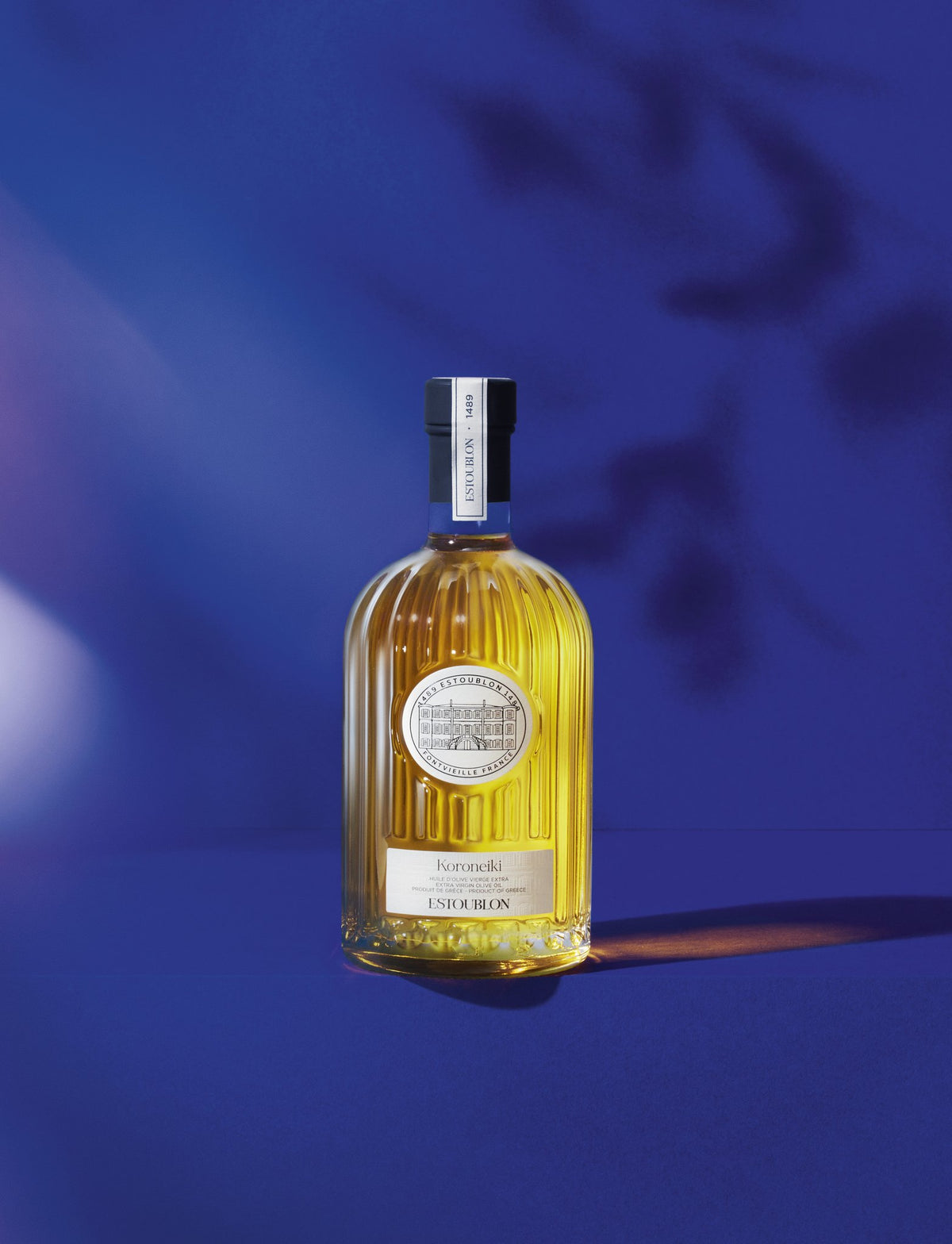 Koroneiki single-variety olive oil by Château d'Estoublon, styled on a blue background