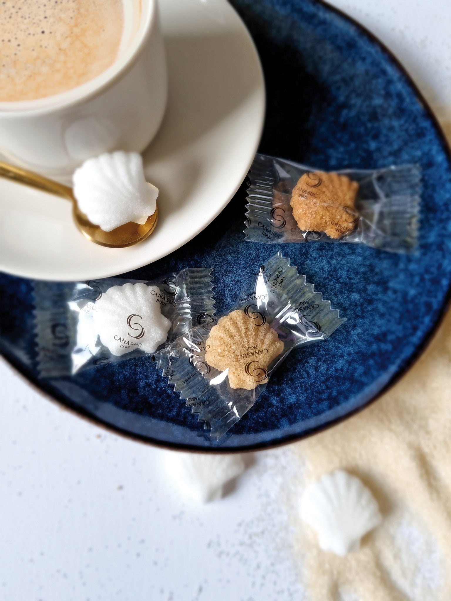 Sucres en coquille Saint-Jacques Prendre le large Canasuc dans leurs sachets individuels, à côté d’un café