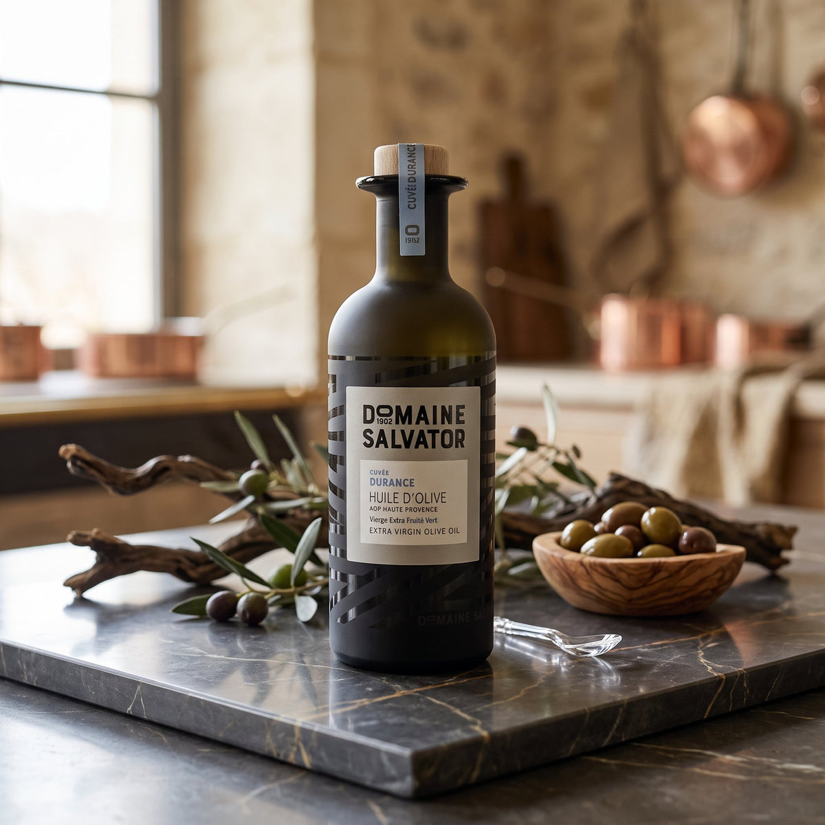 Domaine Salvator Durance olive oil on a marble counter with olives and olive branches