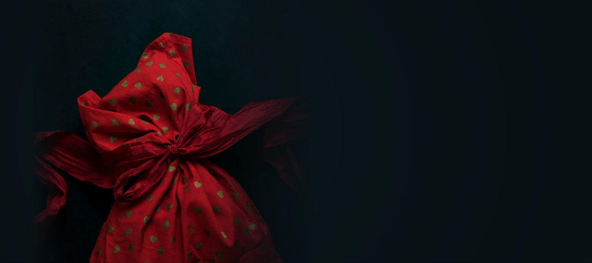 Red gift bag with gold hearts tied with a red ribbon on a dark background
