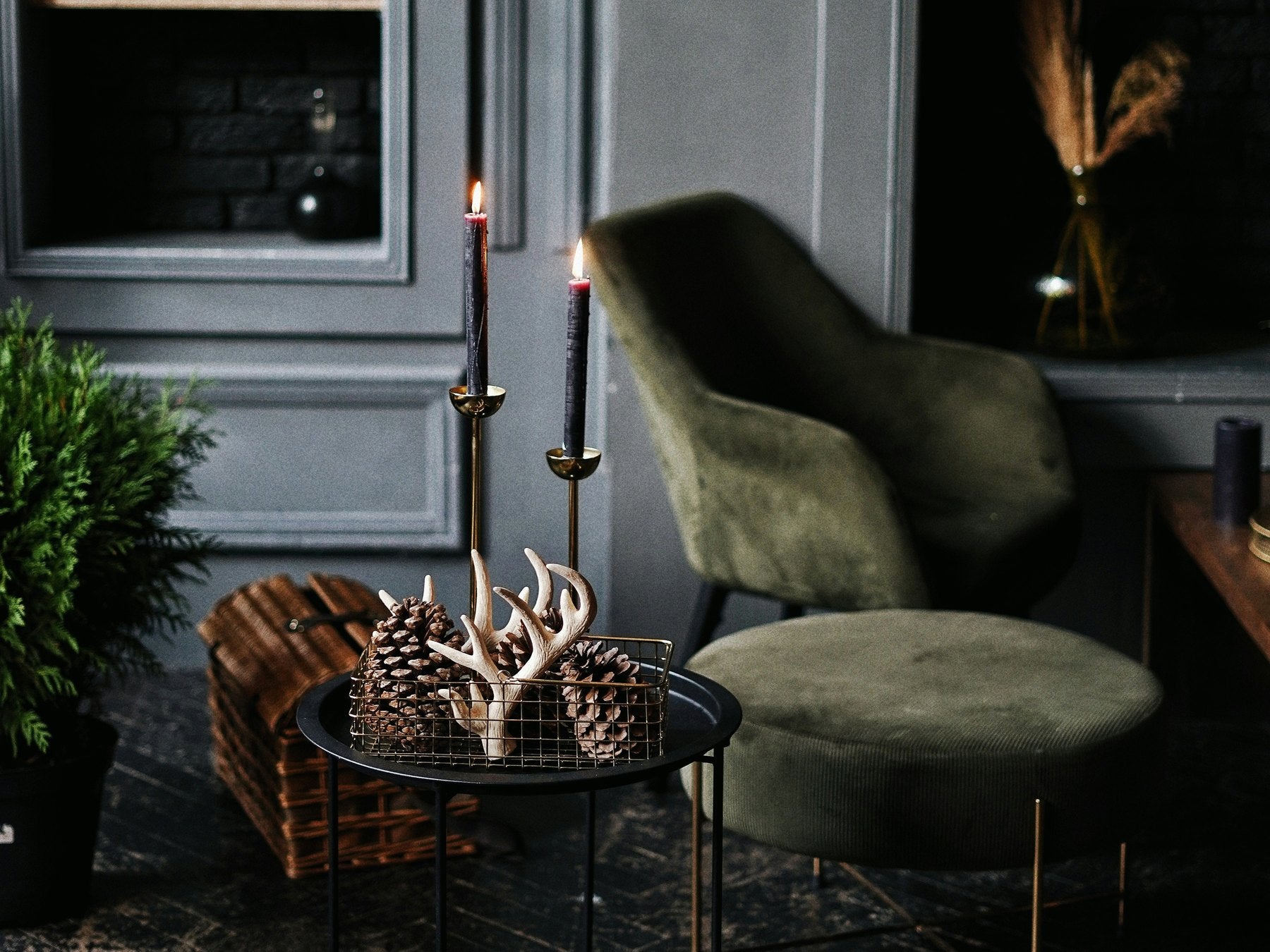 Candlelit living room with a green velvet armchair and pine cones